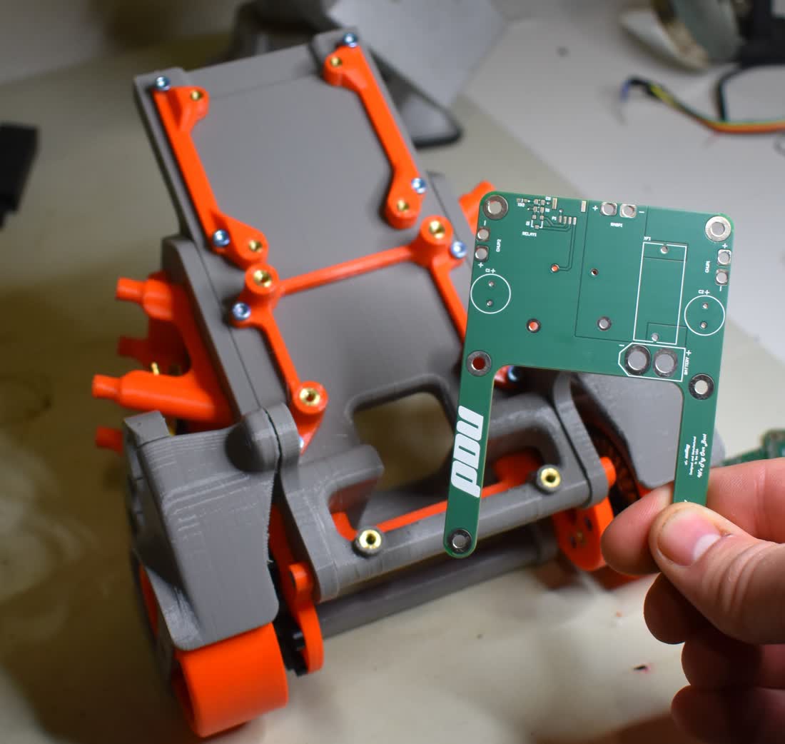 A hand fitting a circuit board into a 3D-printed robot chassis on a workbench